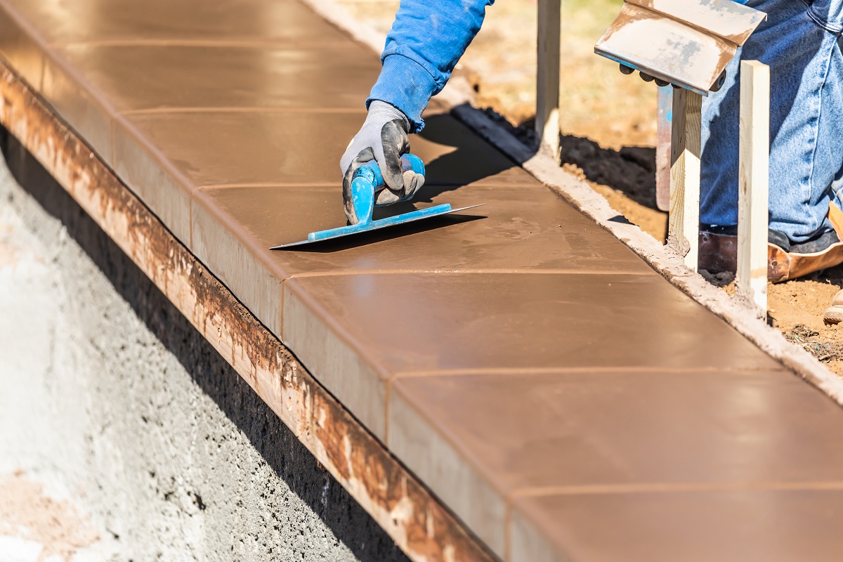 Construction Worker Using Trowel On Wet Cement Forming Coping Around New Pool.